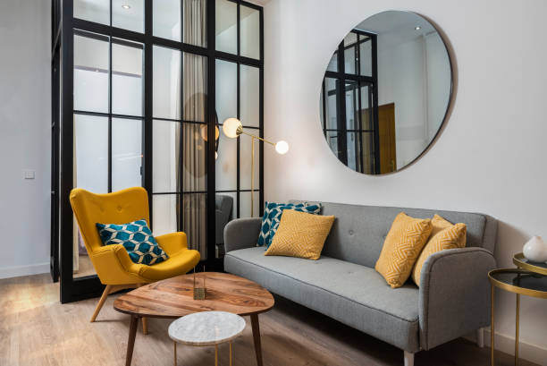 Colorful and cozy living room with a designer armchair and sofa along with a round decorative mirror and glass wall.